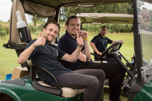 men giving thumbs up whilst sat in a golf caddy